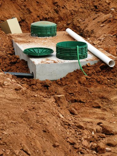 Green septic tank lids beside a white PVC pipe in an excavated dirt pit