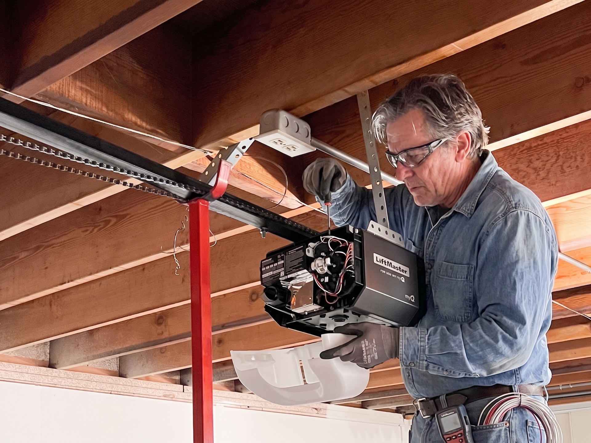 Man installing a garage door opener under wooden beams with a power tool