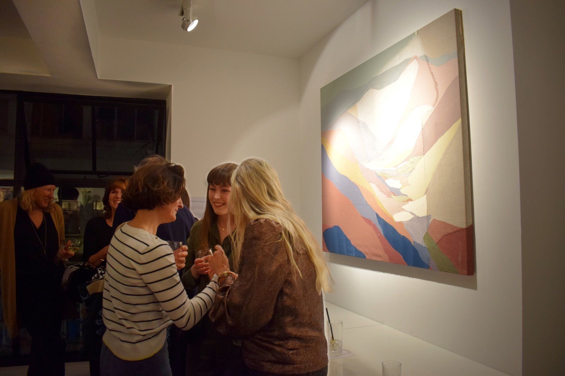 Photo of three people standing in front of a colourful abstract painting on a white gallery wall