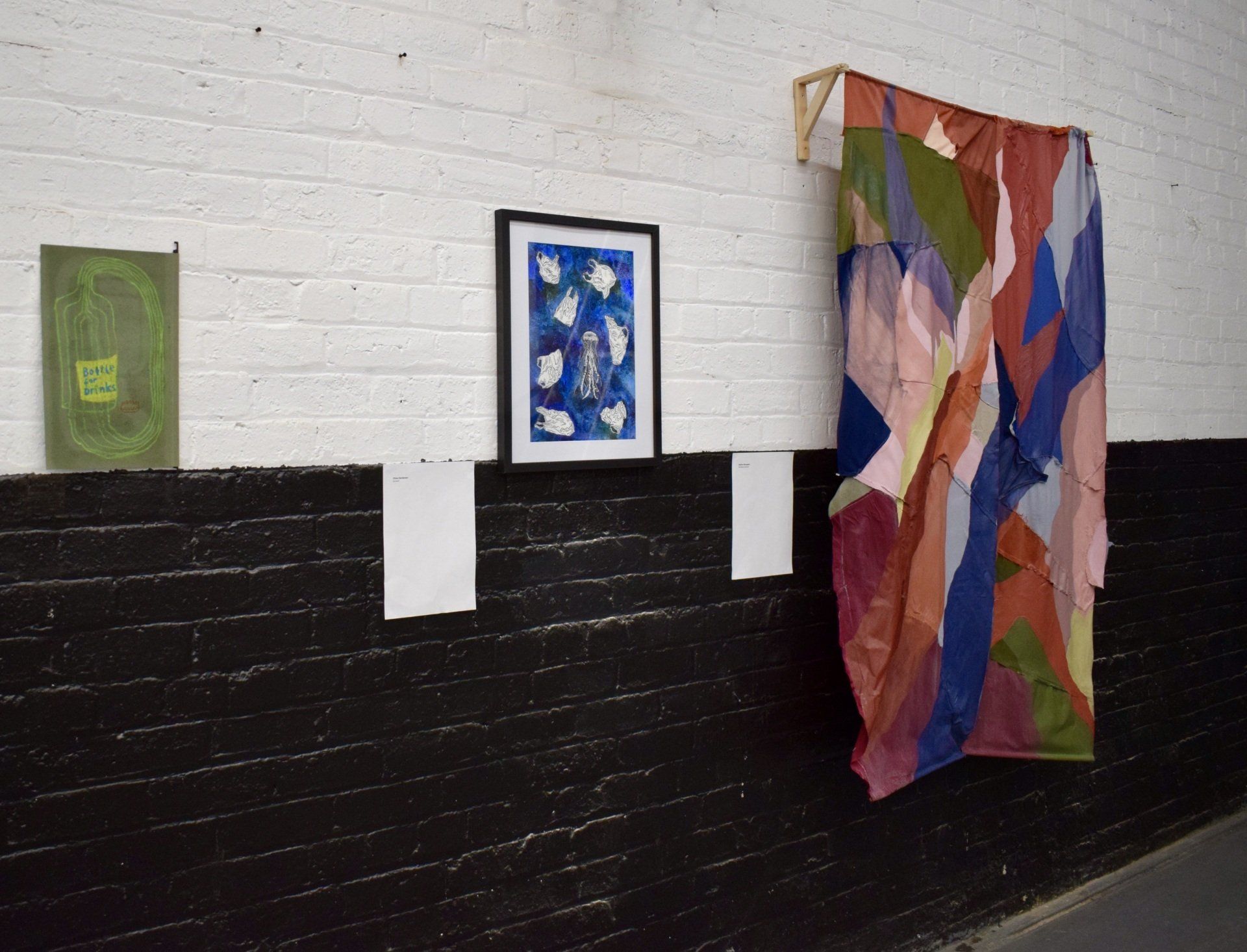Three paintings hanging on wall painting half white with black bricks underneath