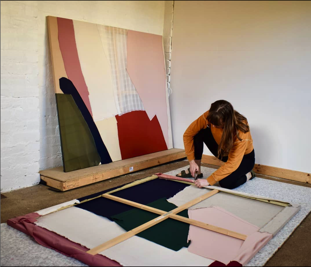 Photo of artist working in a studio with white walls and a painting on the ground