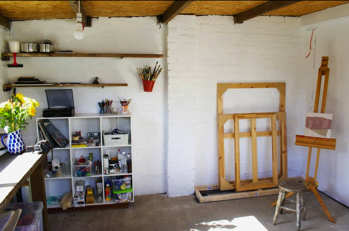 Photo of artist studio with white walls and wooden ceiling. Showing artist tools and frames
