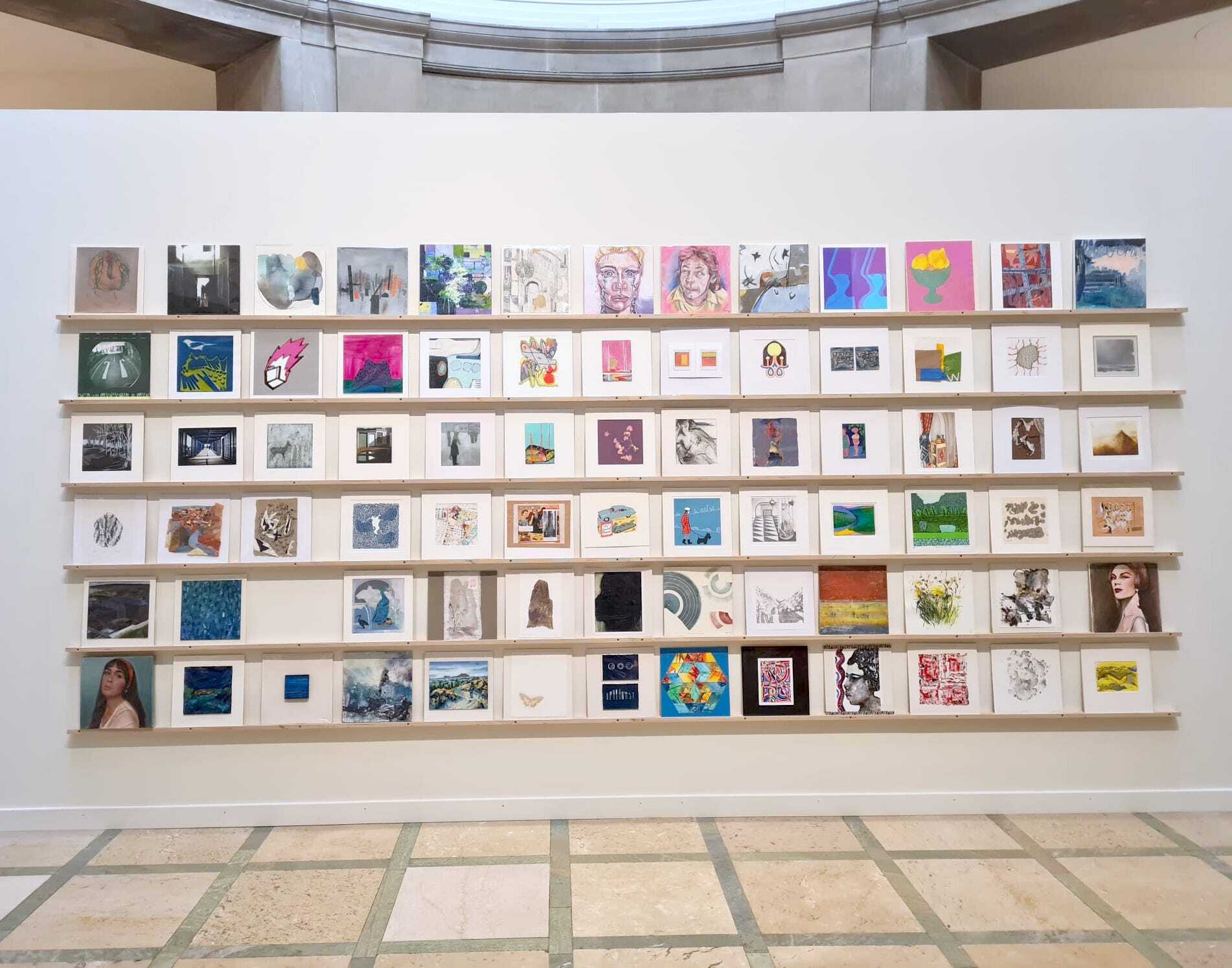 White wall with 6 shelves displaying small artworks