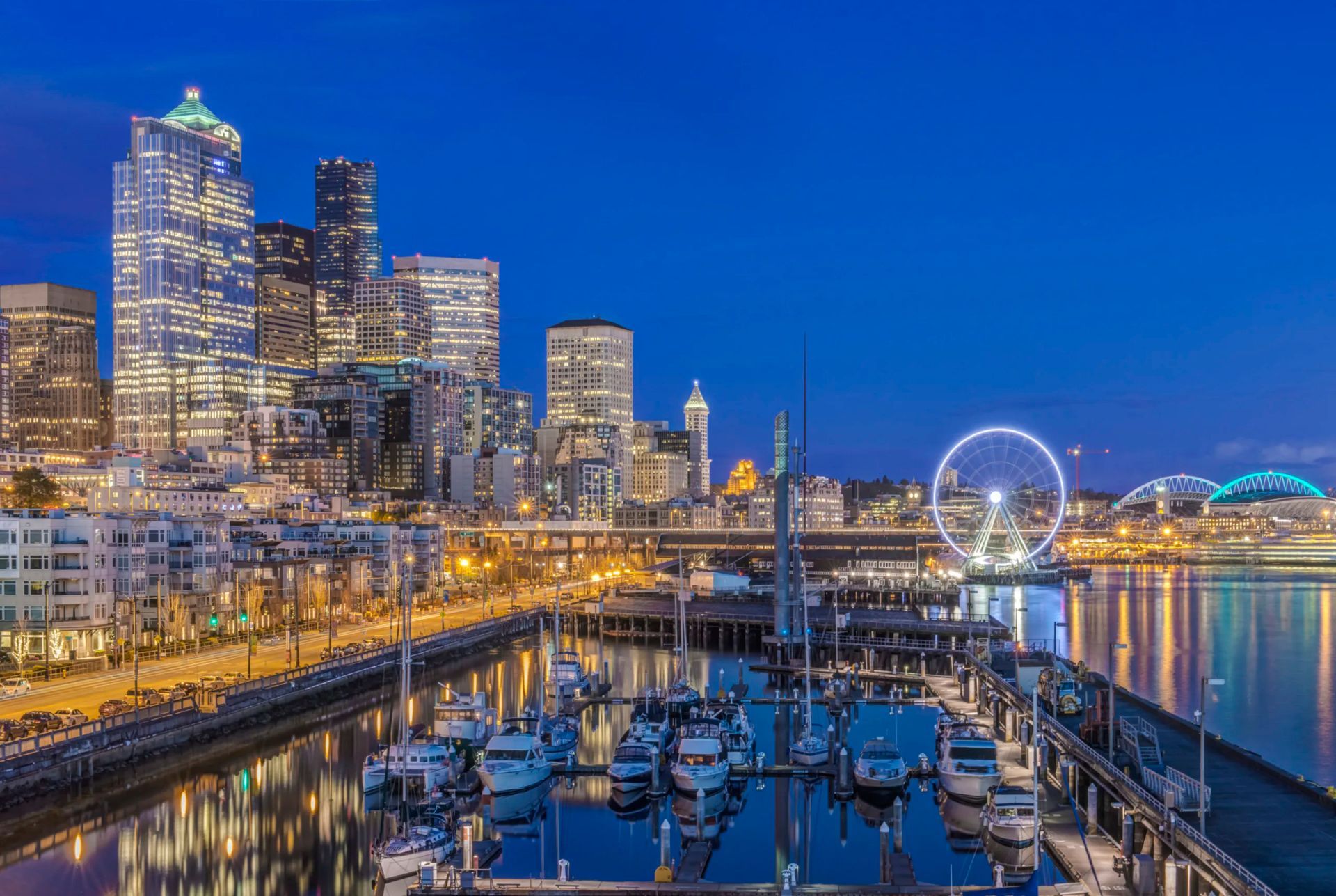 Seattle waterfront at dusk, with city skyline, ferris wheel, boats, and dark blue sky.