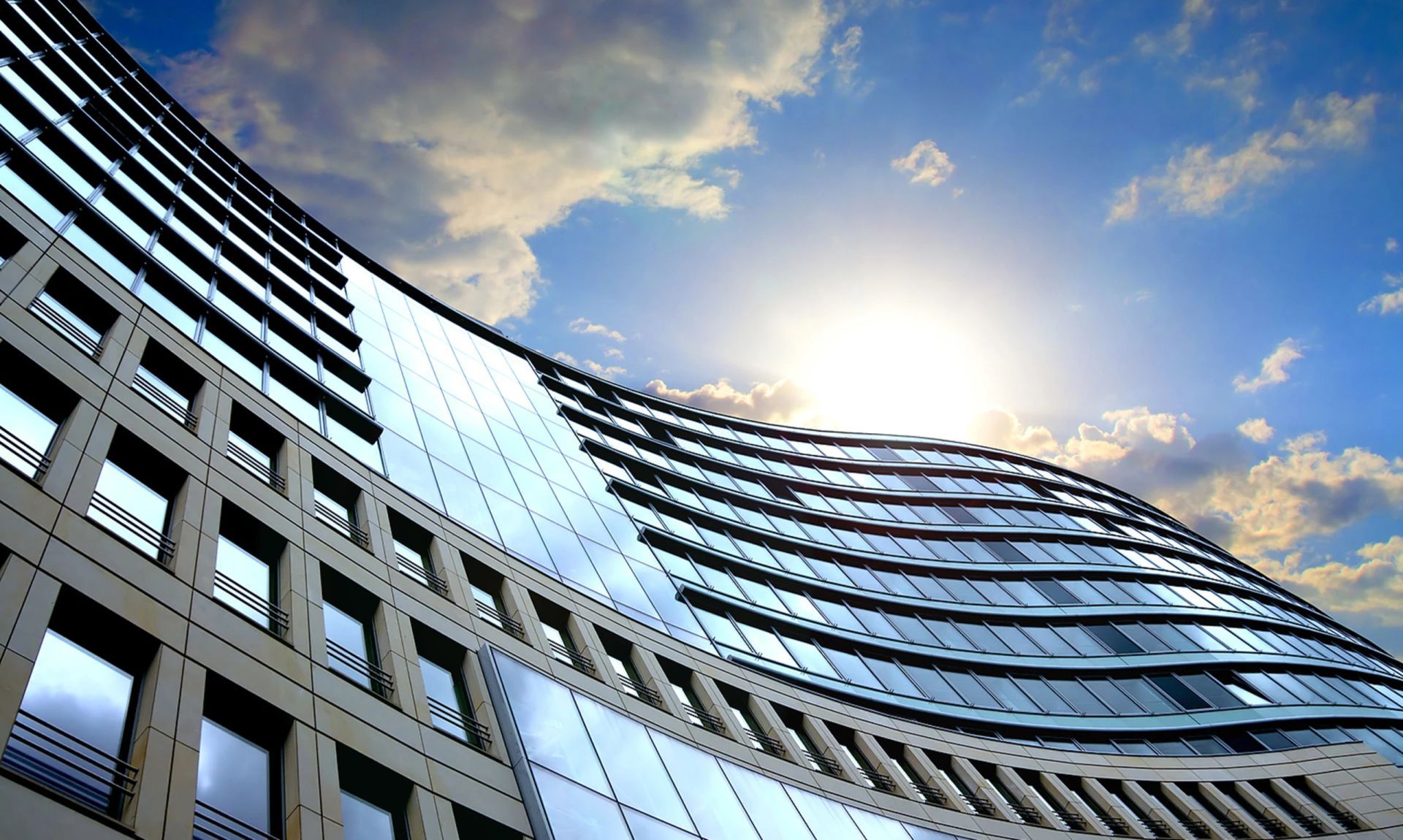 Modern curved building with reflective glass facade against a sunny, cloudy sky.