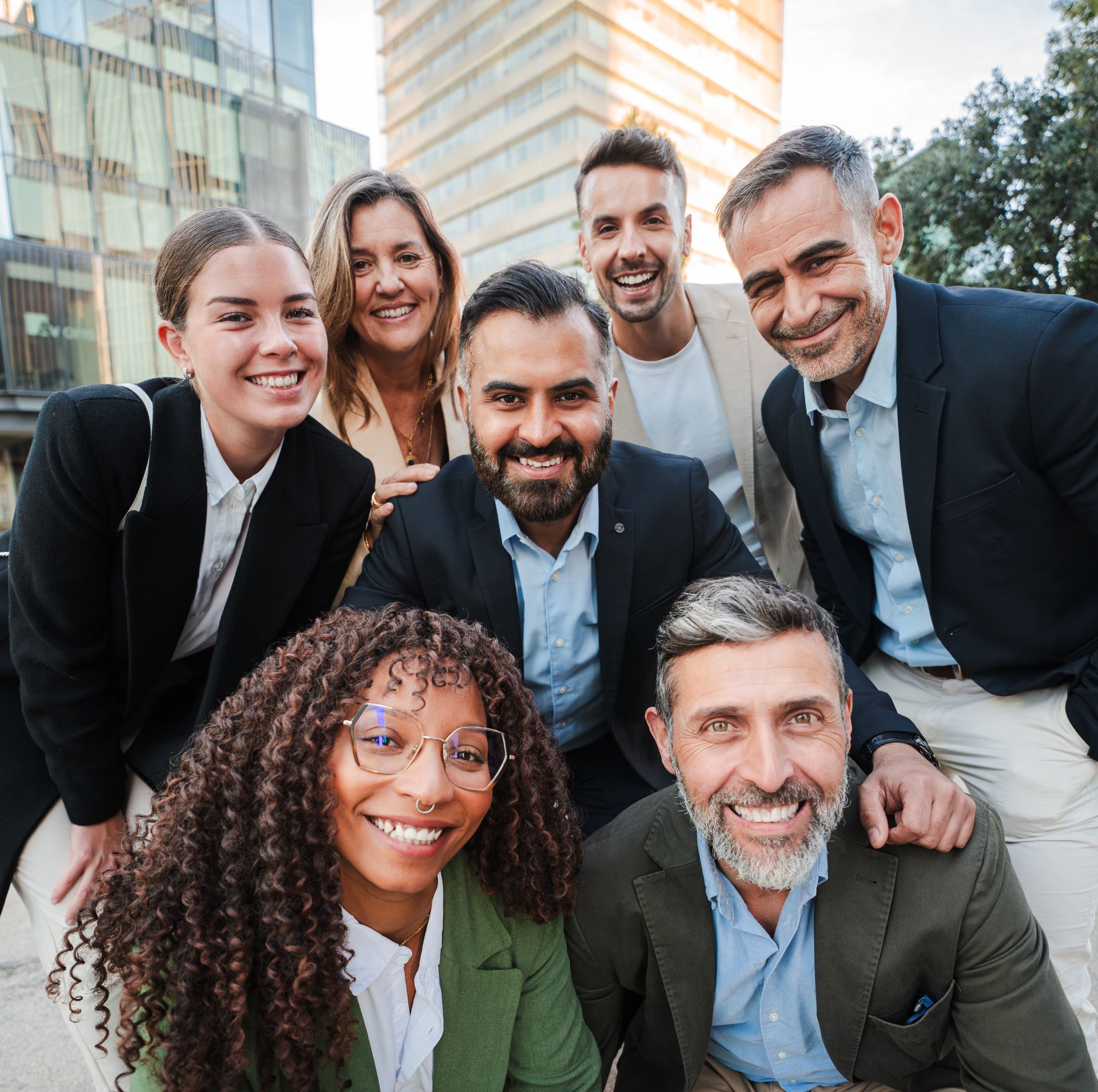 Group of diverse coworkers smiling for a photo outdoors, near a modern building.