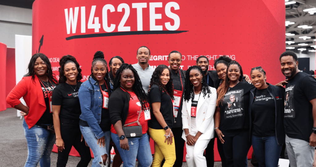 Group of people smiling, posing in front of a red backdrop with white text