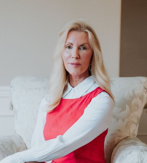 Woman in red top and white collared shirt seated in a patterned chair, looking forward.
