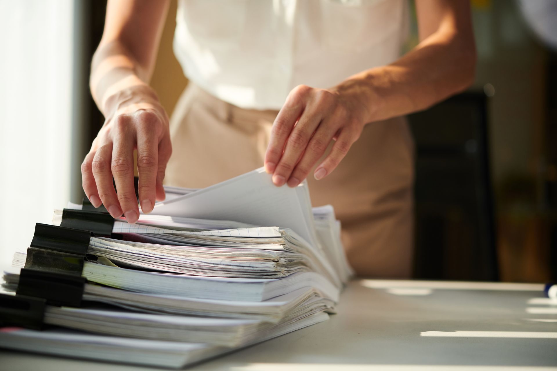 Hands sorting through a large stack of papers, clipped together, on a desk in an office.