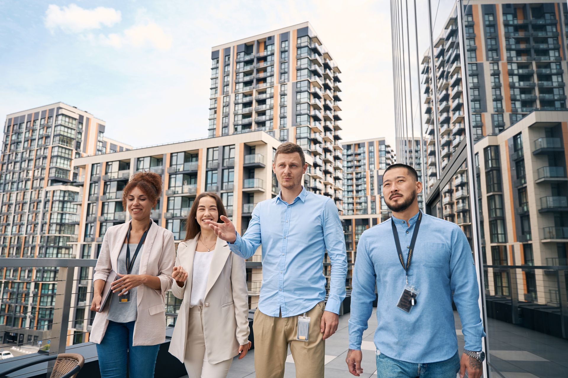 Four people walking outside, smiling. City buildings in the background, one person waving.