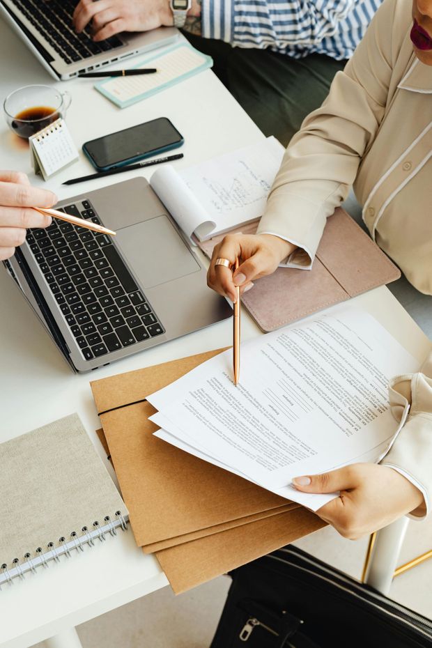 People reviewing documents and working on laptops at a white desk.
