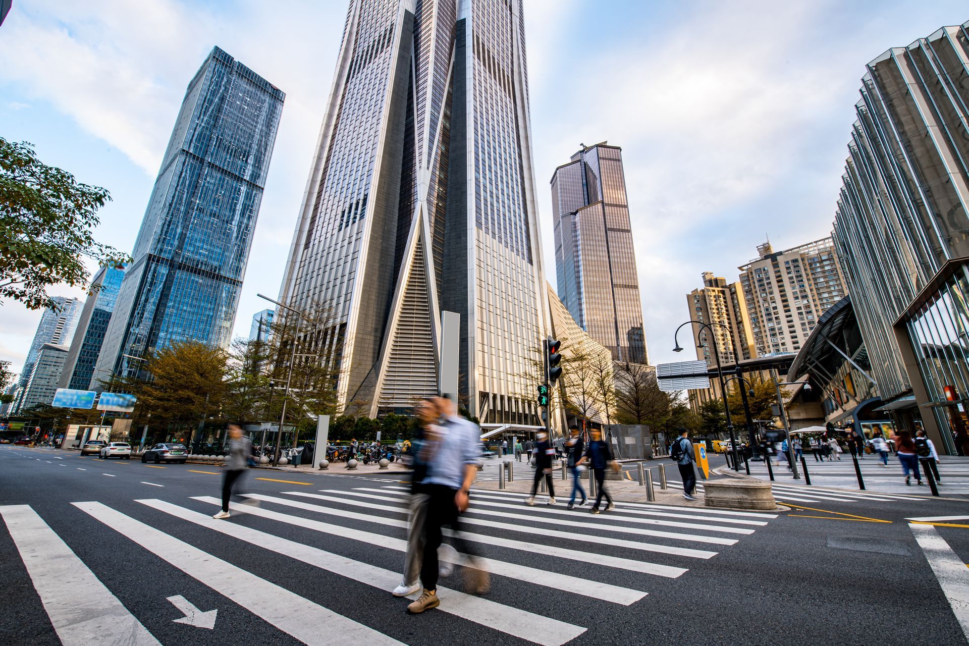 People crossing a street with a zebra crossing, tall modern buildings in background.