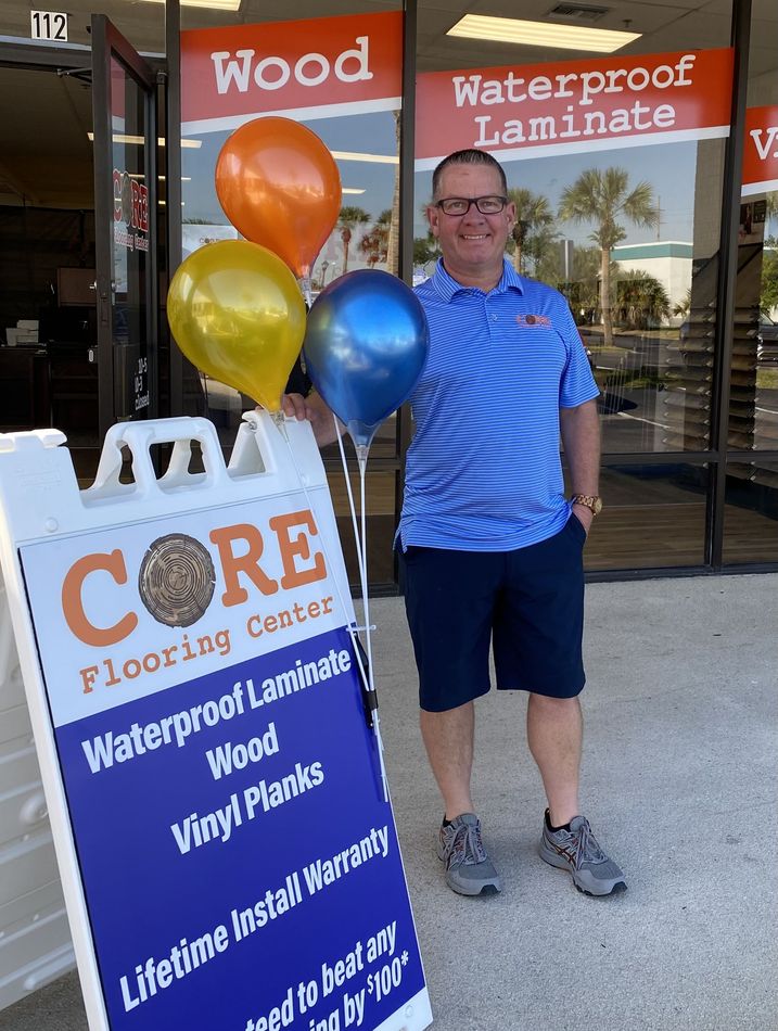 A man holding balloons in front of a core flooring center