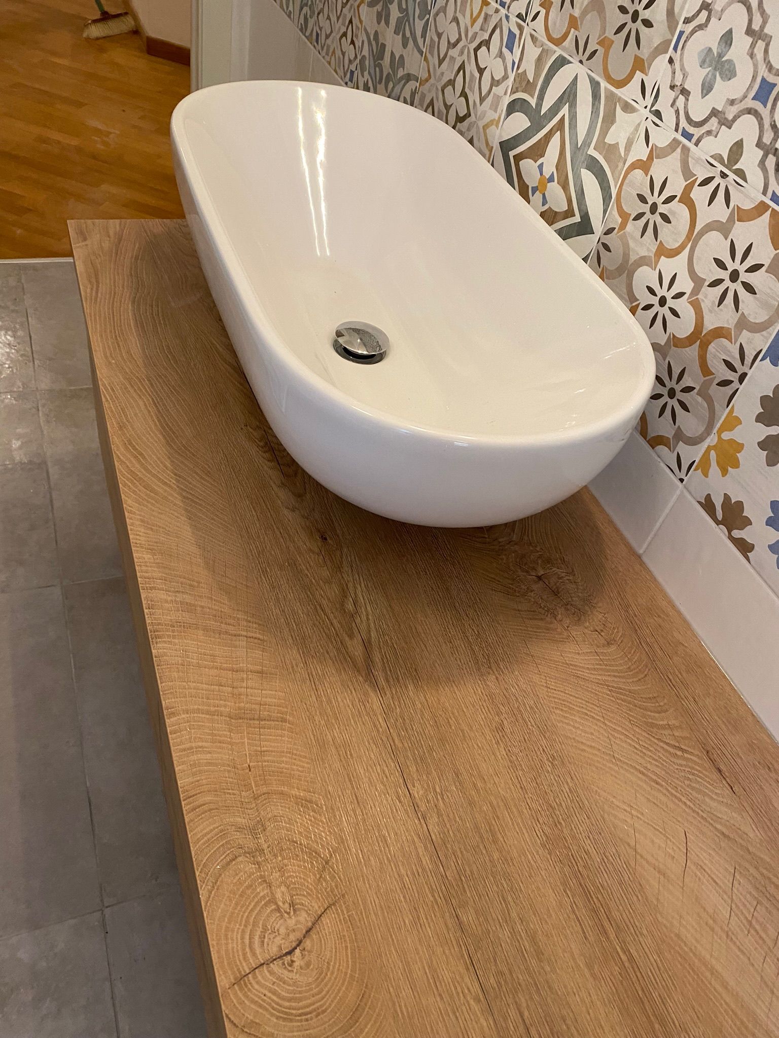 In un bagno c'è un lavandino bianco appoggiato su un ripiano di legno.
