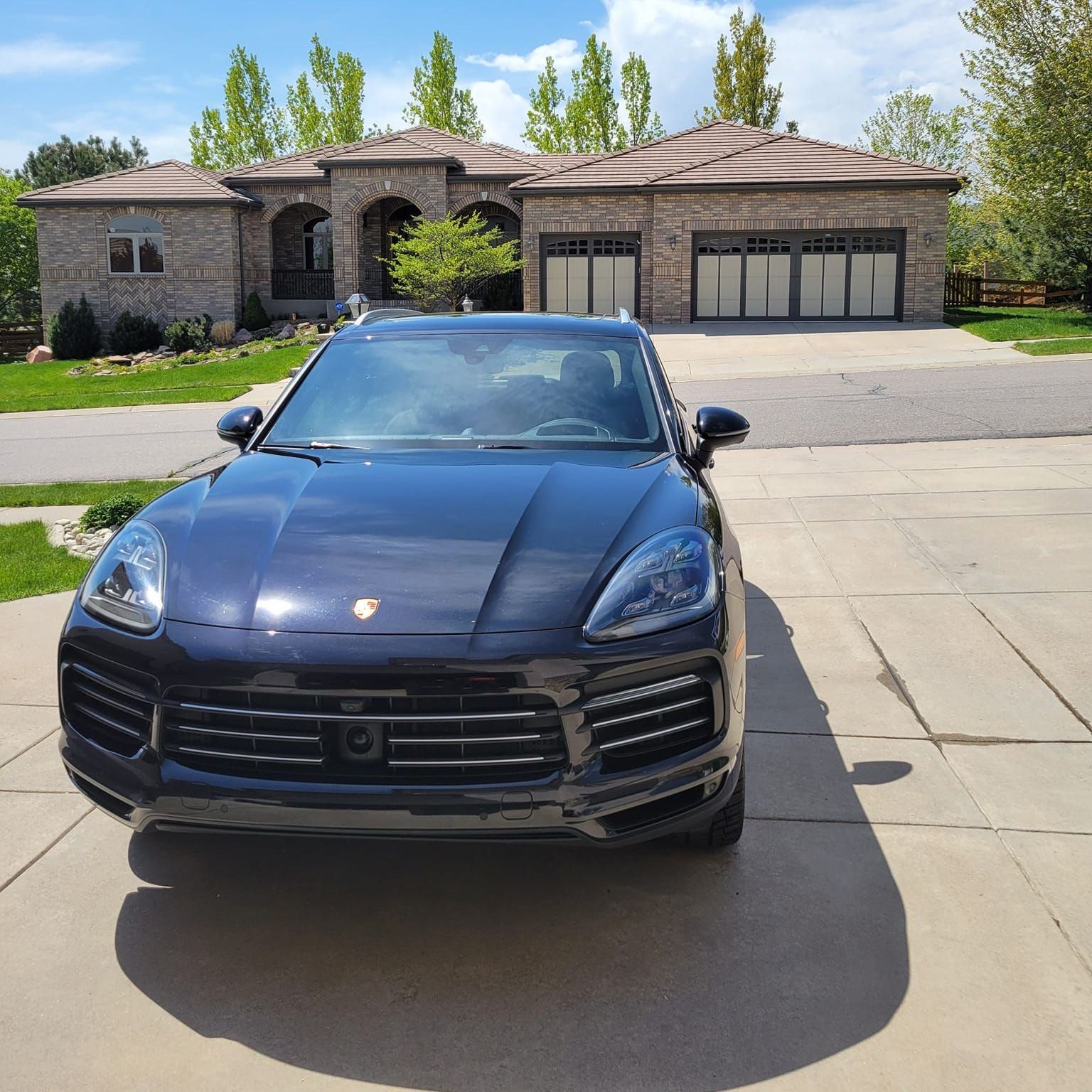 A black car is parked in front of a large house