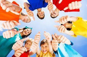 A group of children wearing colorful shirts form a circle, looking down and giving thumbs-up gestures against a blue sky.