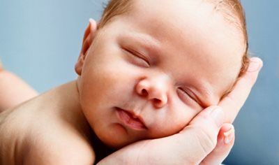 Sleeping baby resting on a hand, eyes closed, with a soft blue background