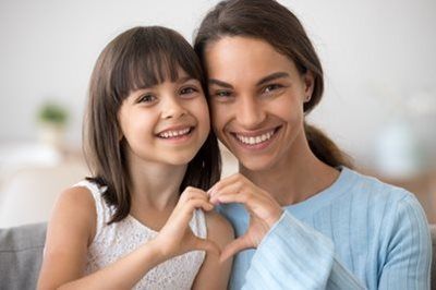 Smiling woman and child making a heart shape with their hands on a couch