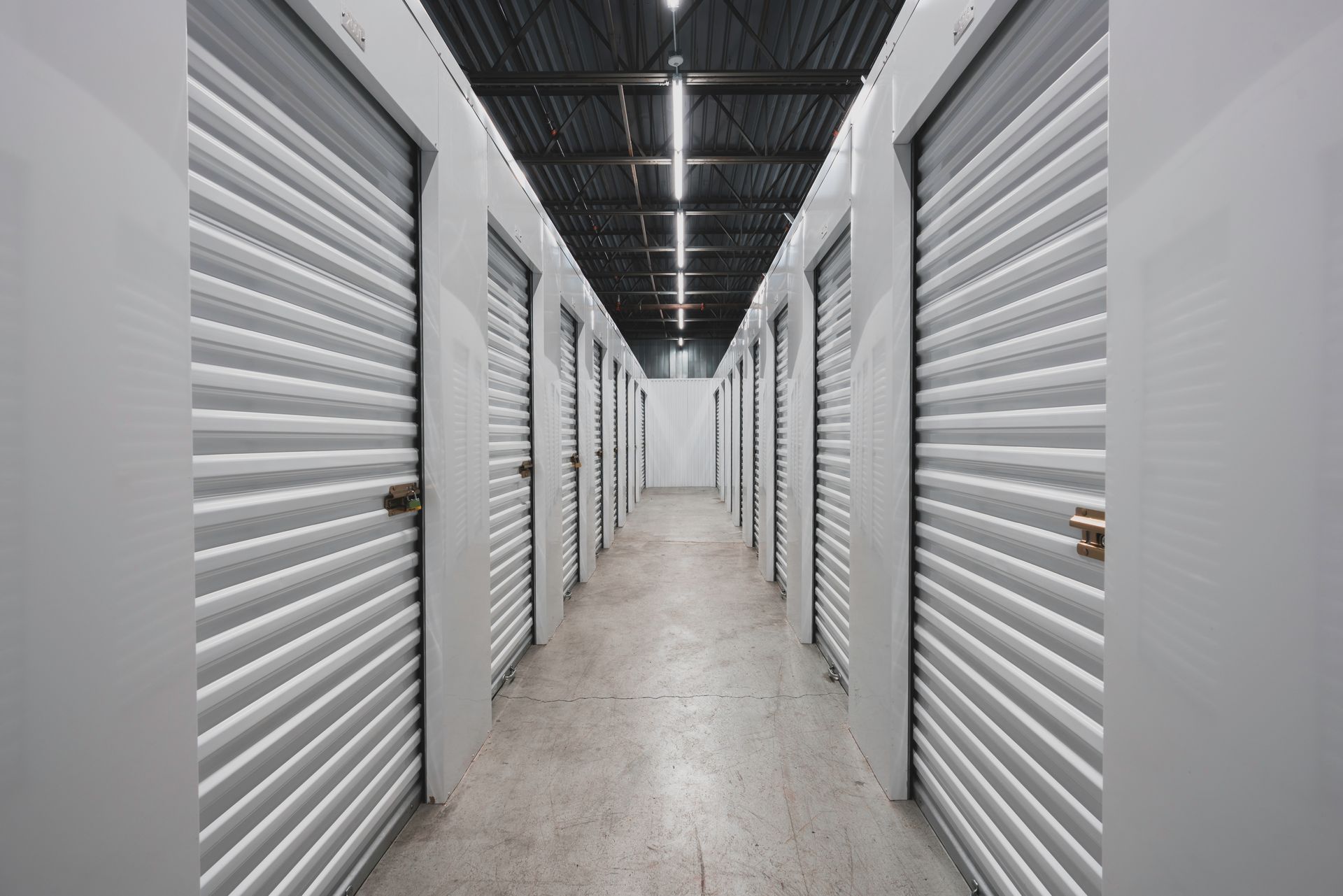 Self storage units with secure roll-up doors along a clean, well-lit indoor storage hallway.