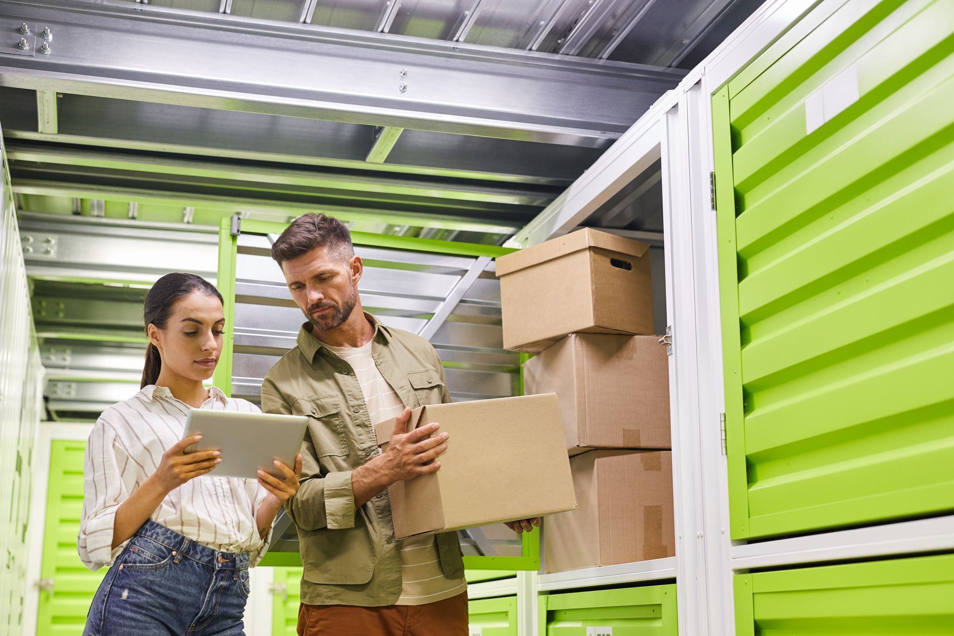Two coworkers using a digital tablet while loading boxes into a self-storage container. Two coworkers using a digital tablet while loading boxes into a self-storage container.