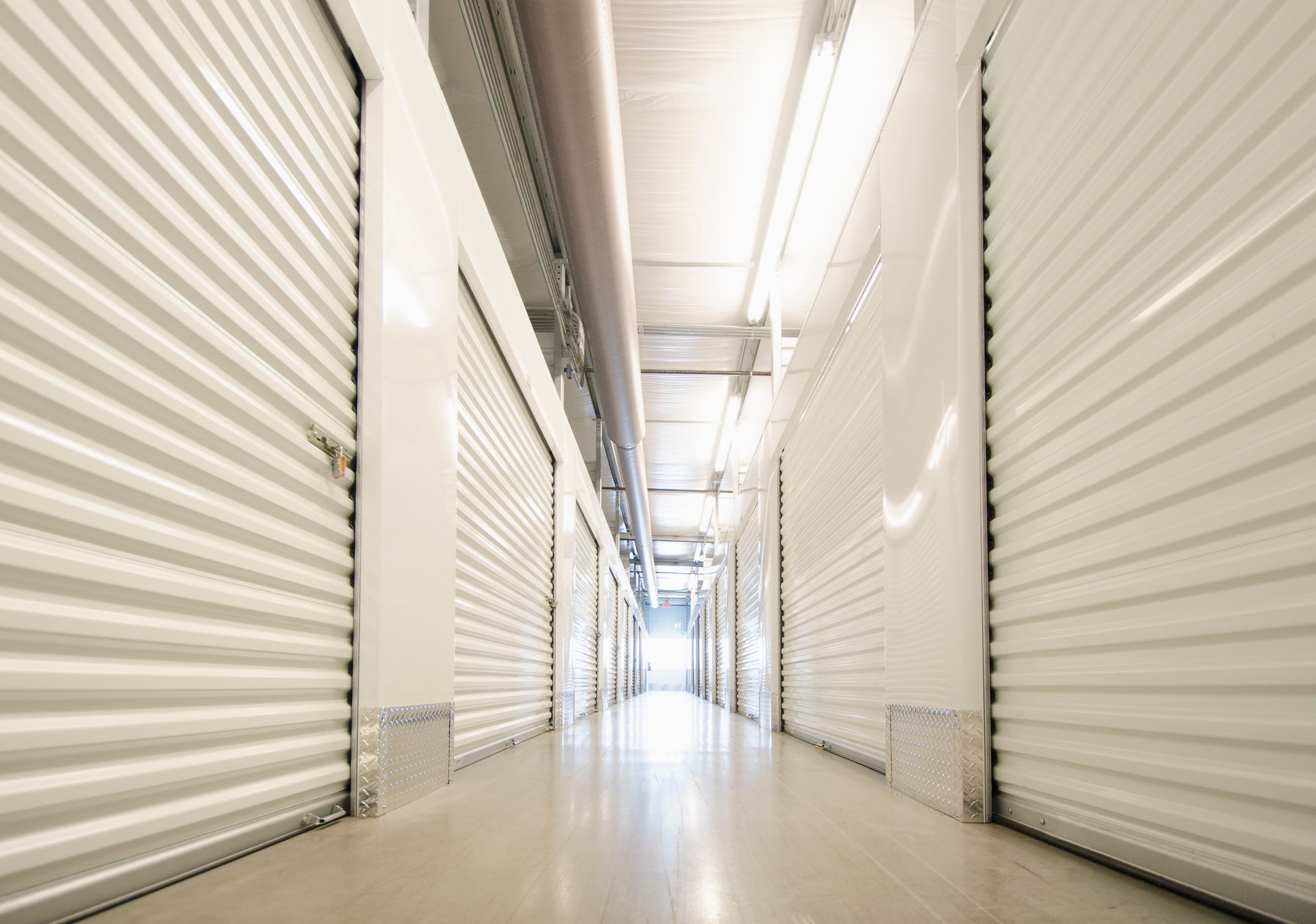 Bright hallway lined with closed white metal storage unit doors.