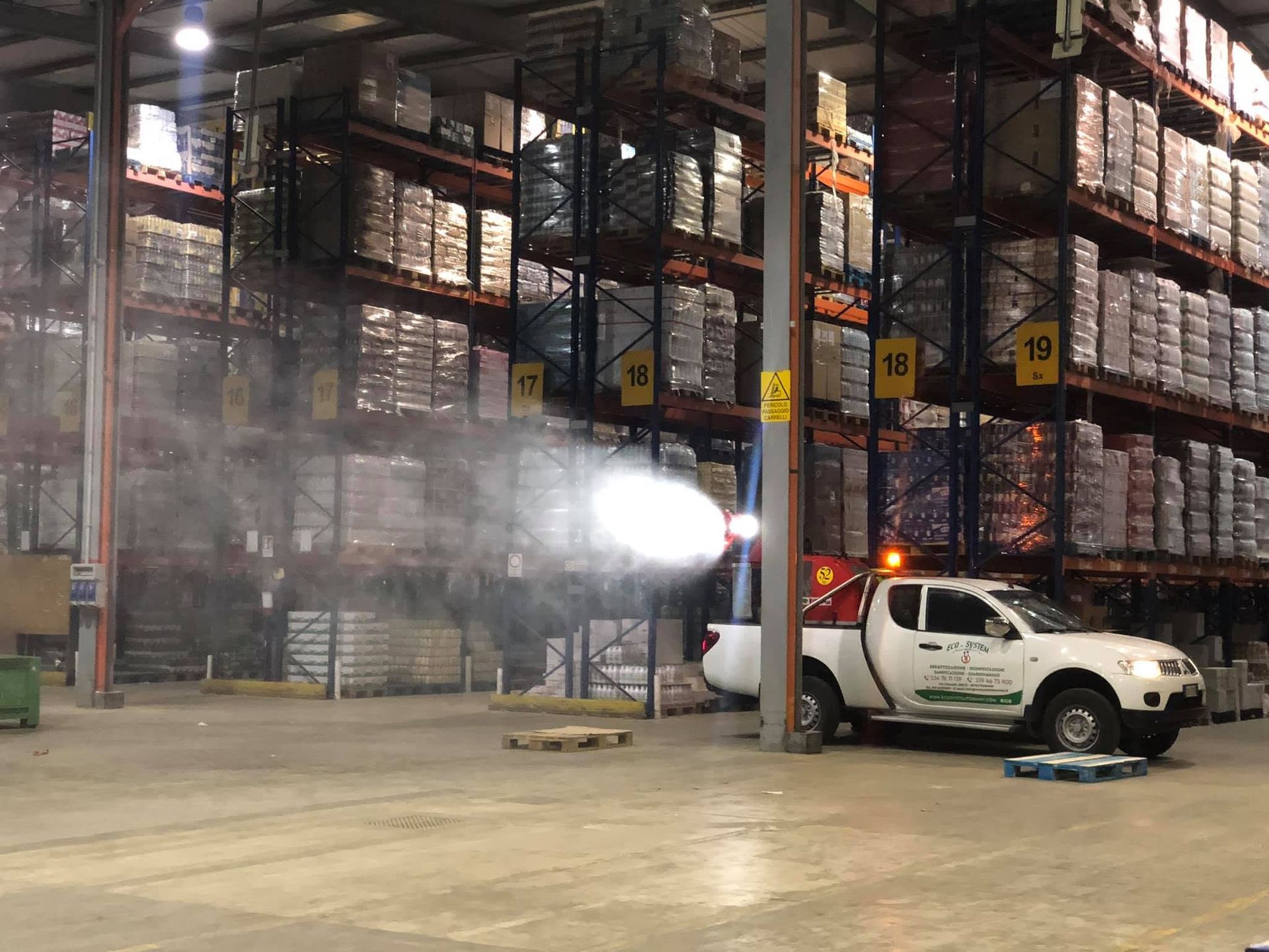 Magazzino con un pick-up bianco che spruzza fumo o nebbia all'interno degli scaffali di stoccaggio.