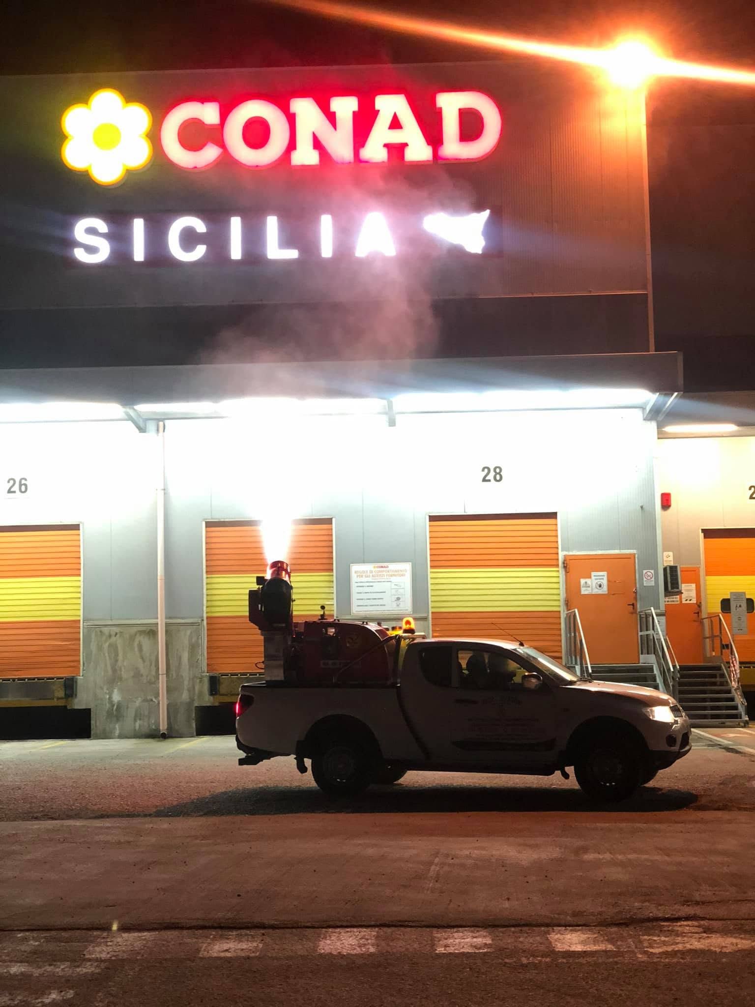 La vetrina del negozio Conad Sicilia di notte, con un pick-up parcheggiato all'esterno sotto luci intense.