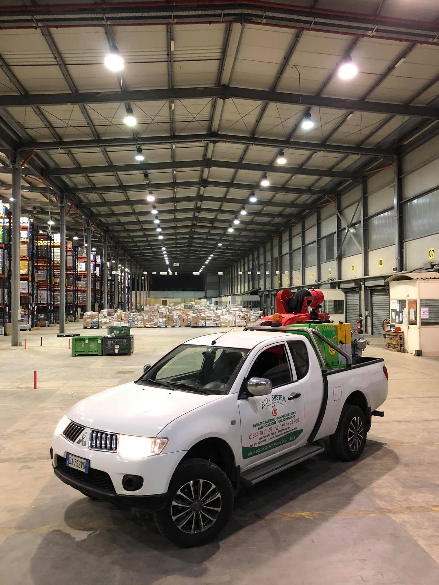 Un pick-up bianco all'interno di un grande magazzino con scaffali alti e luci intense a soffitto.