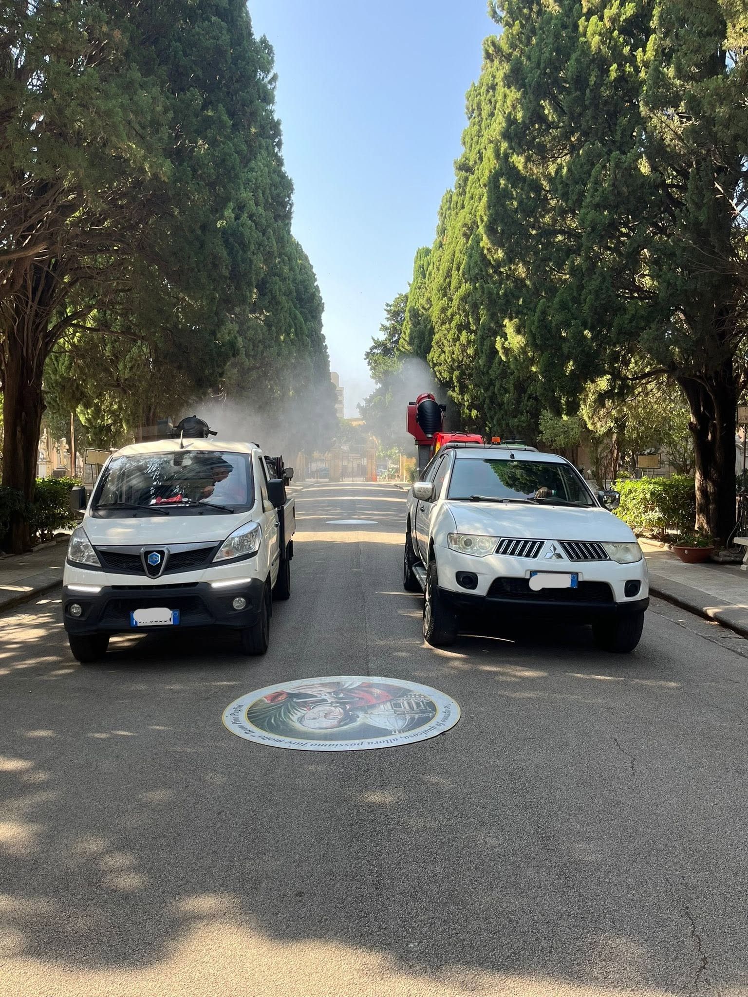 Due SUV bianchi su una strada alberata, con spruzzi d'acqua sullo sfondo e una persona in piedi tra di loro.