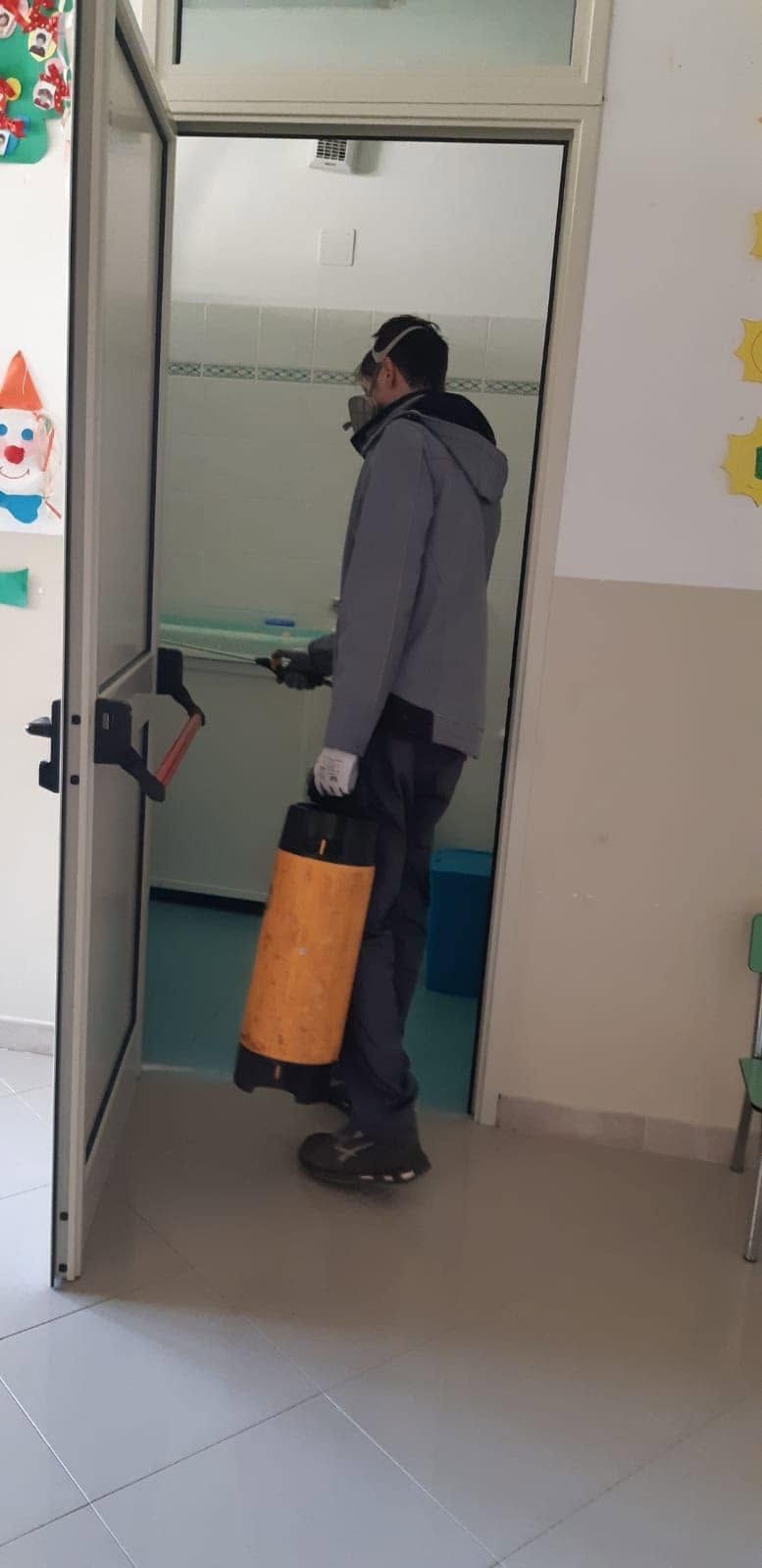 Una persona si trova sulla soglia di una porta di un corridoio e tiene in mano una valigia arancione.