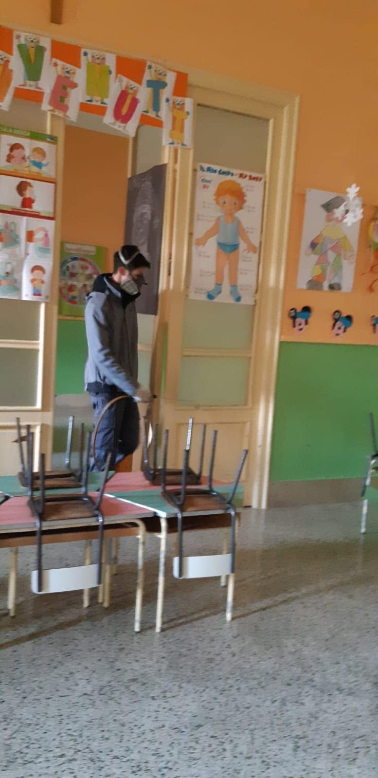 Una persona in piedi su una sedia in un'aula colorata, vicino a una porta e a dei poster alle pareti.