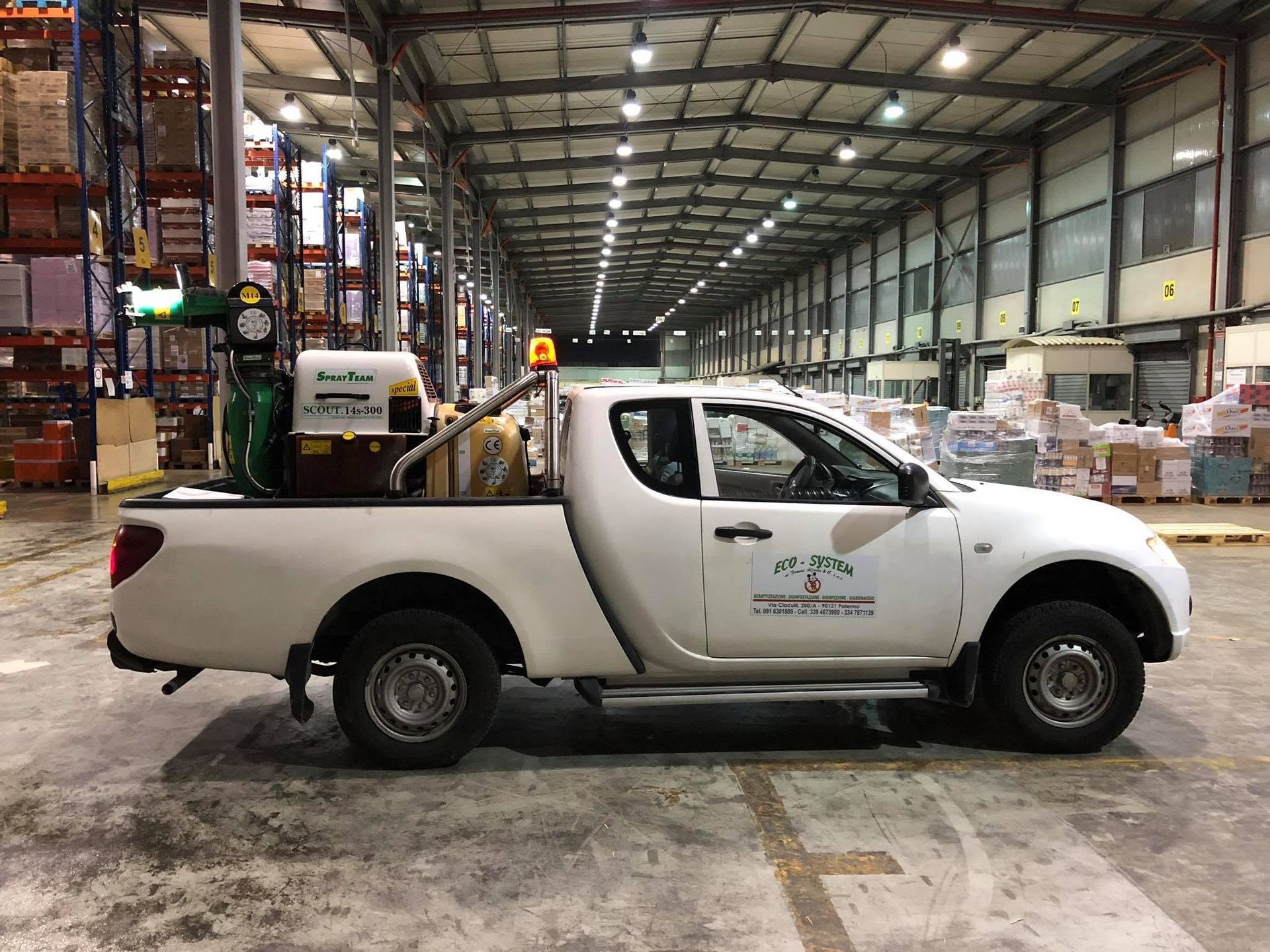 Un pick-up bianco in un magazzino con attrezzature industriali e scaffalature tutt'intorno.