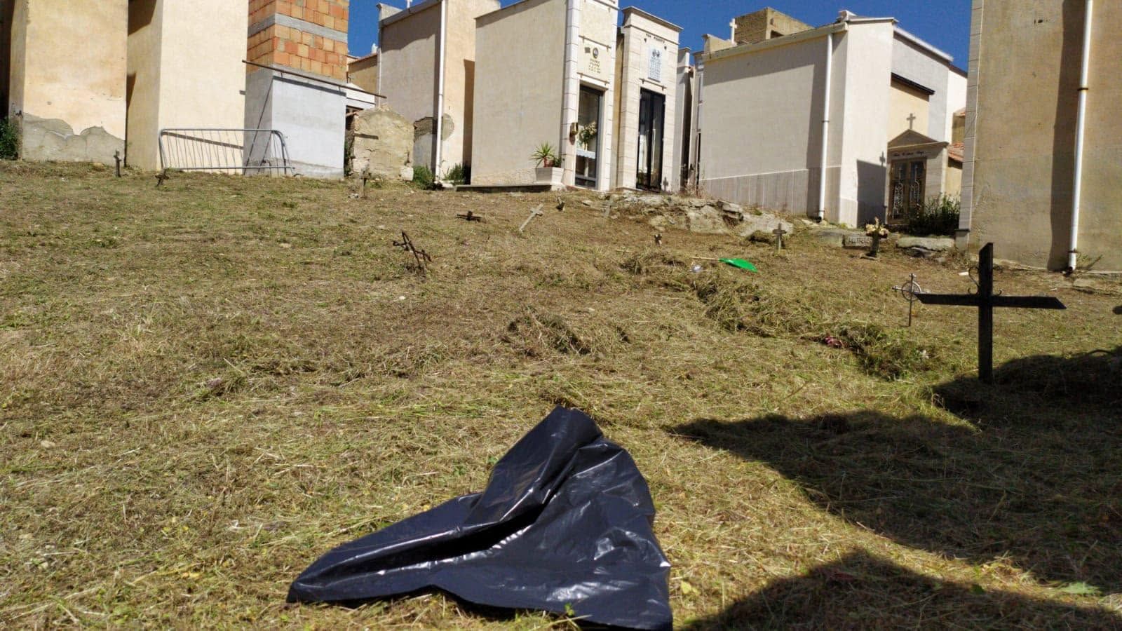 Pendio erboso con un telone nero in primo piano e edifici color sabbia in cima, sotto un cielo limpido.