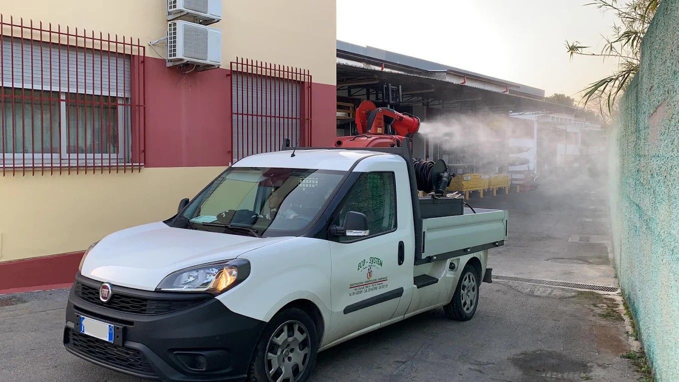 Un camioncino bianco di servizio spruzza acqua da un serbatoio montato a lato di un edificio in una strada stretta.