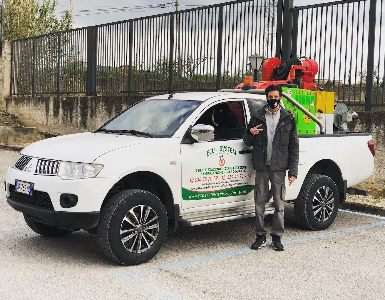 Un uomo è in piedi accanto a un pick-up bianco con dell'attrezzatura caricata sul cassone, a bordo strada.