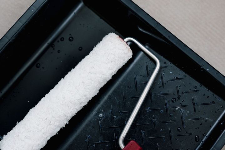 Paint roller with white paint tray on a black surface, wet with droplets.
