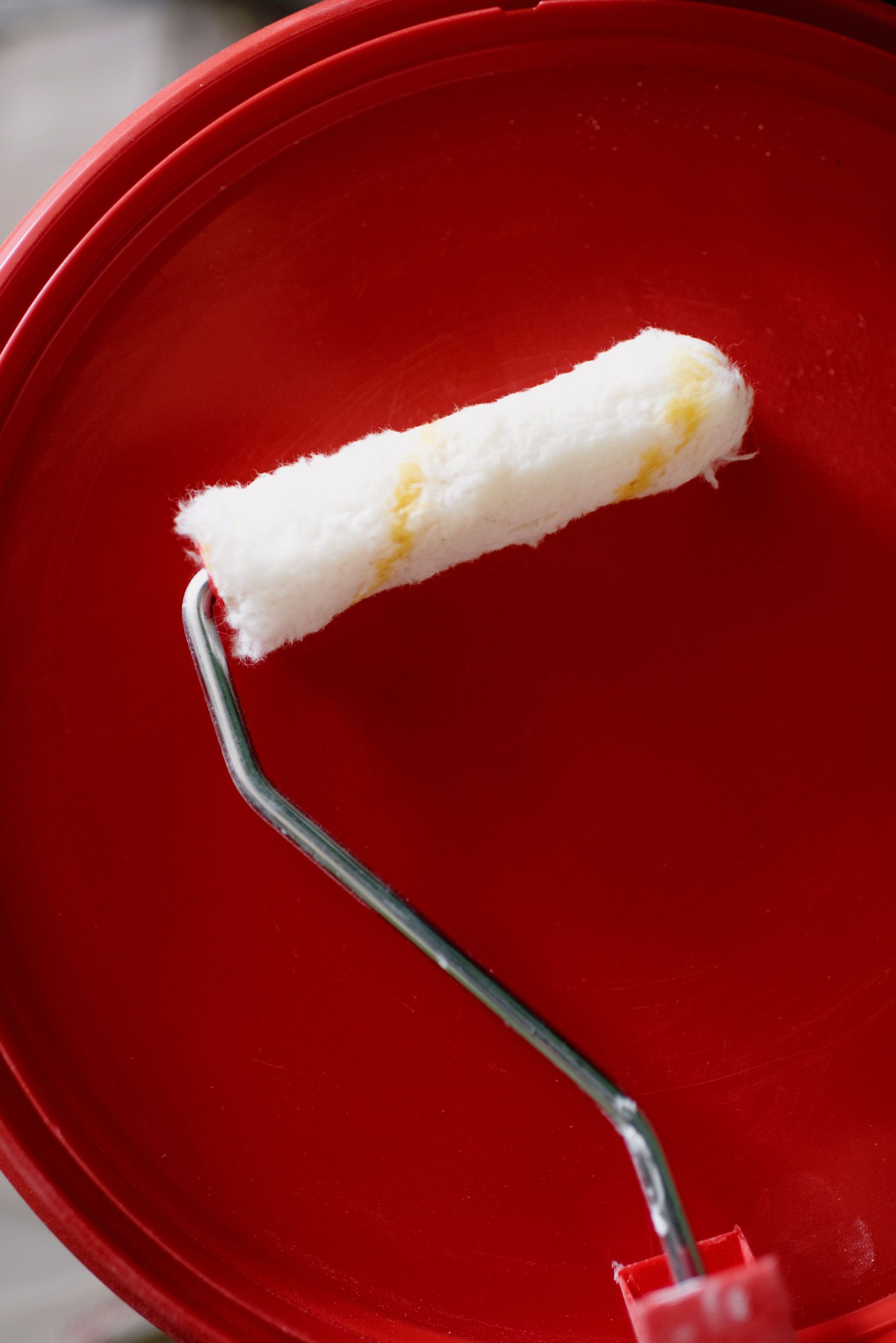 Paint roller loaded with white paint inside a red bucket