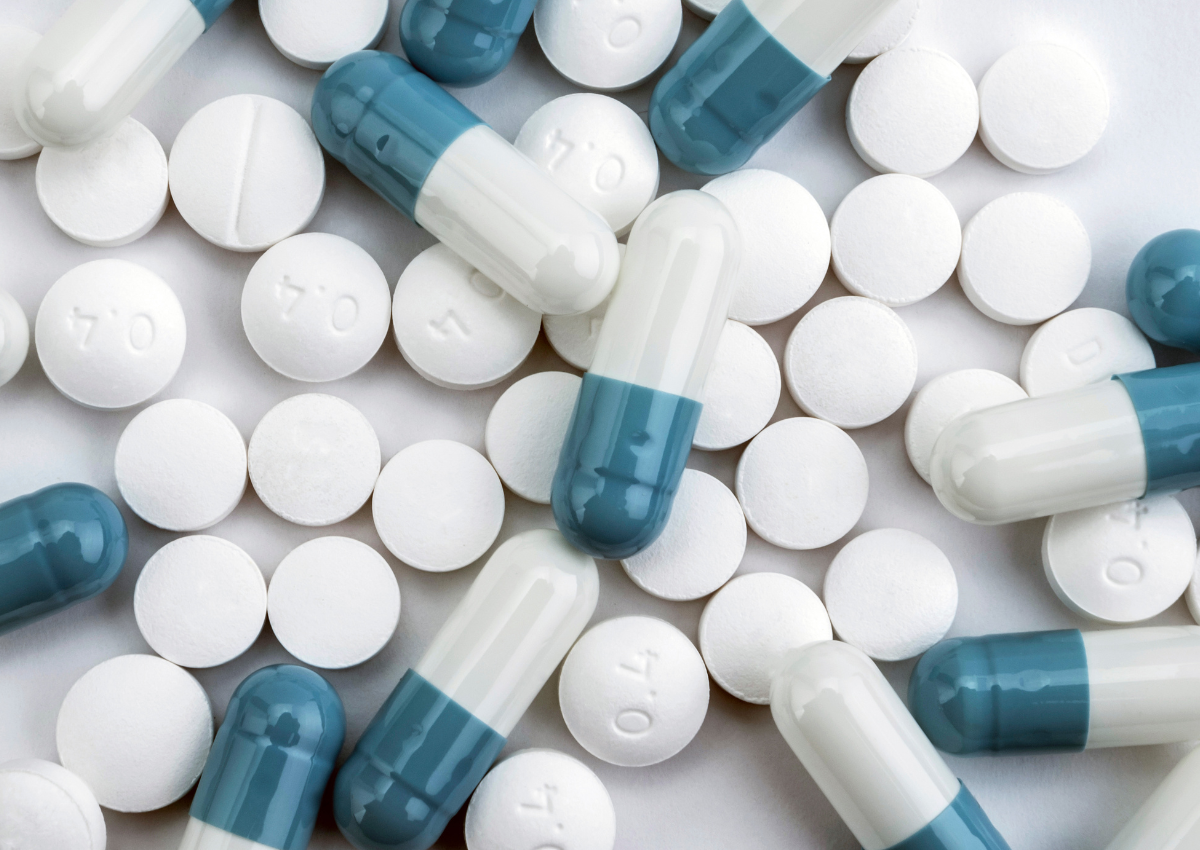 Des pilules blanches et des capsules bleues et blanches dispersées sur une surface blanche.