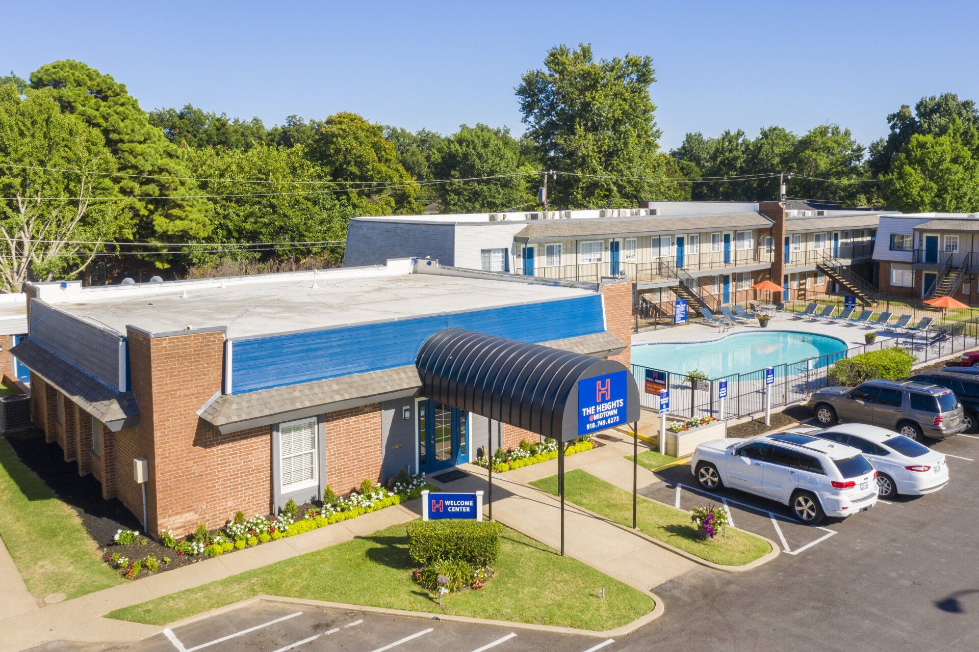 An aerial view of a hotel with a pool and cars parked in front of it.