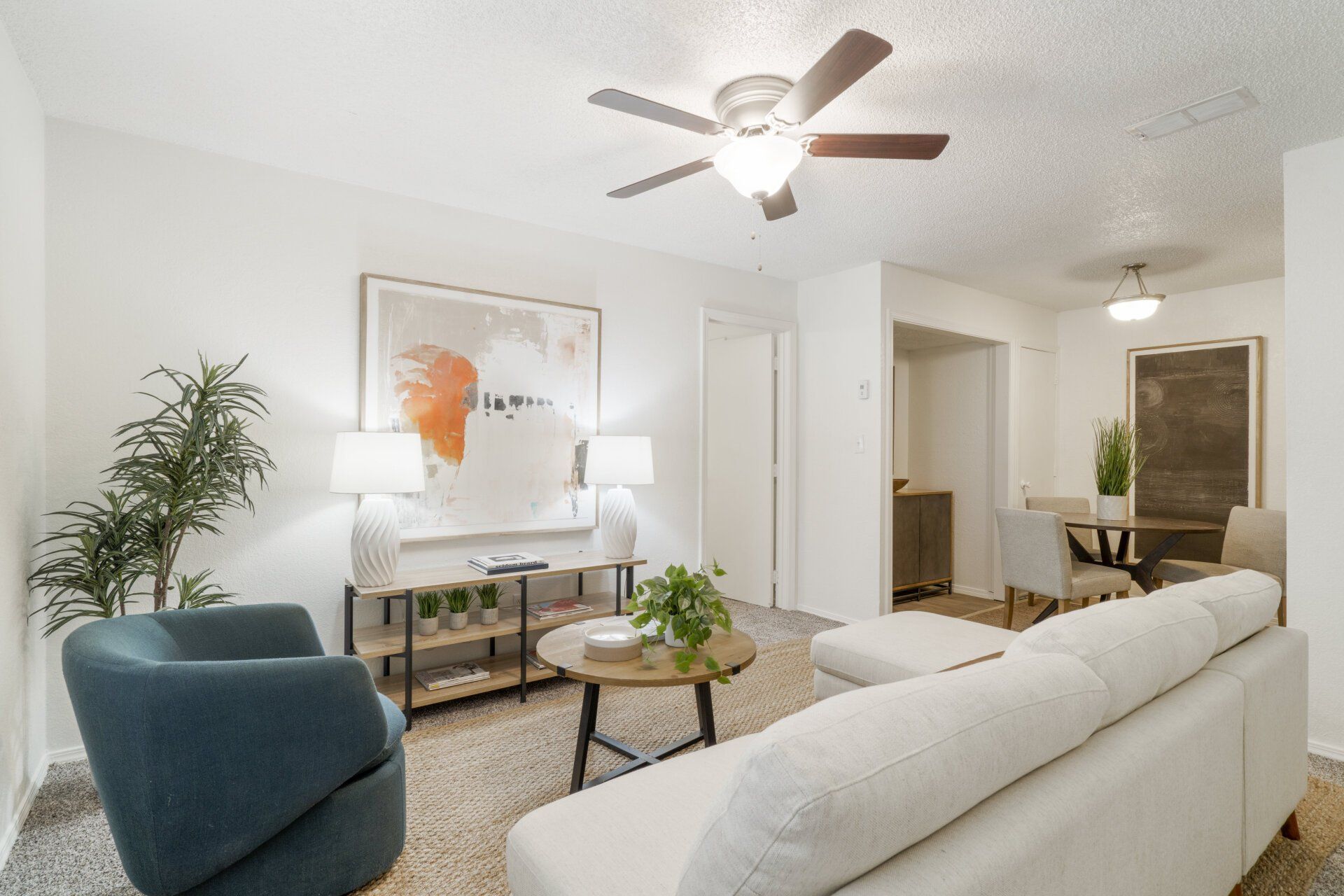 A living room with a couch , chair , coffee table and ceiling fan.