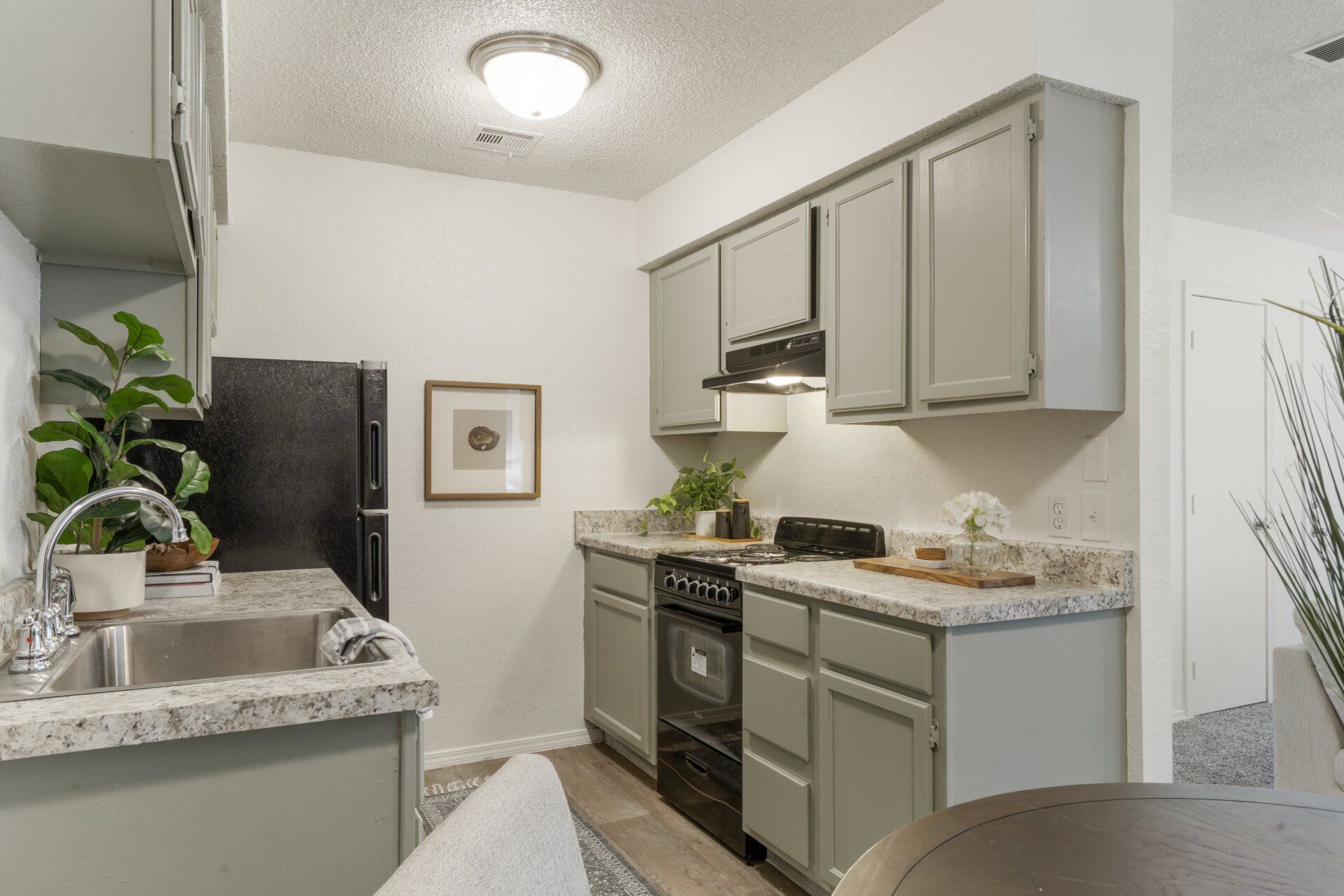 A kitchen with gray cabinets , a black stove , a sink , and a black refrigerator.