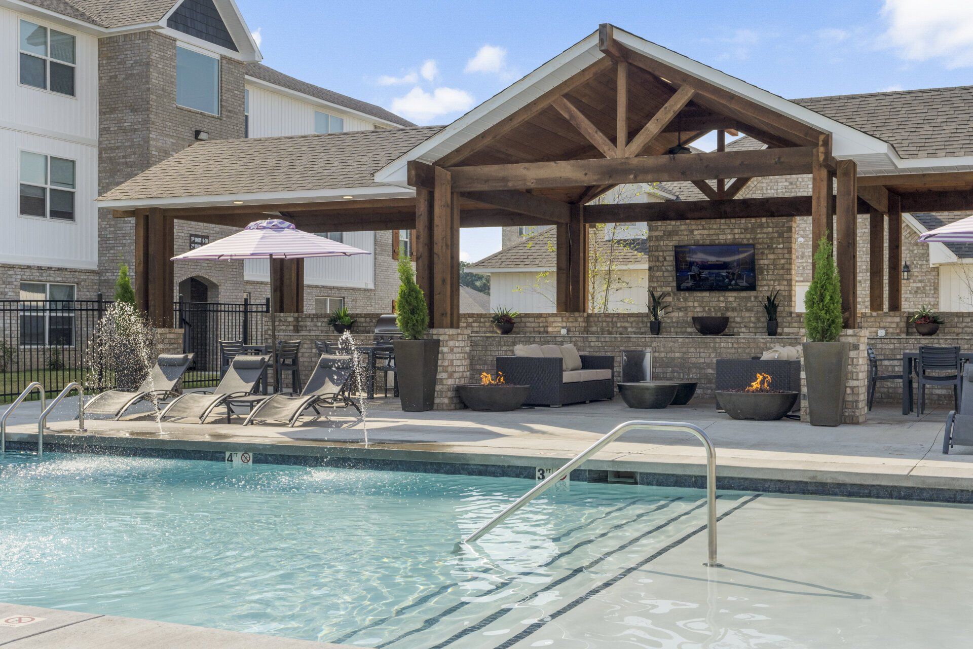 A large swimming pool surrounded by chairs and umbrellas in front of a building.
