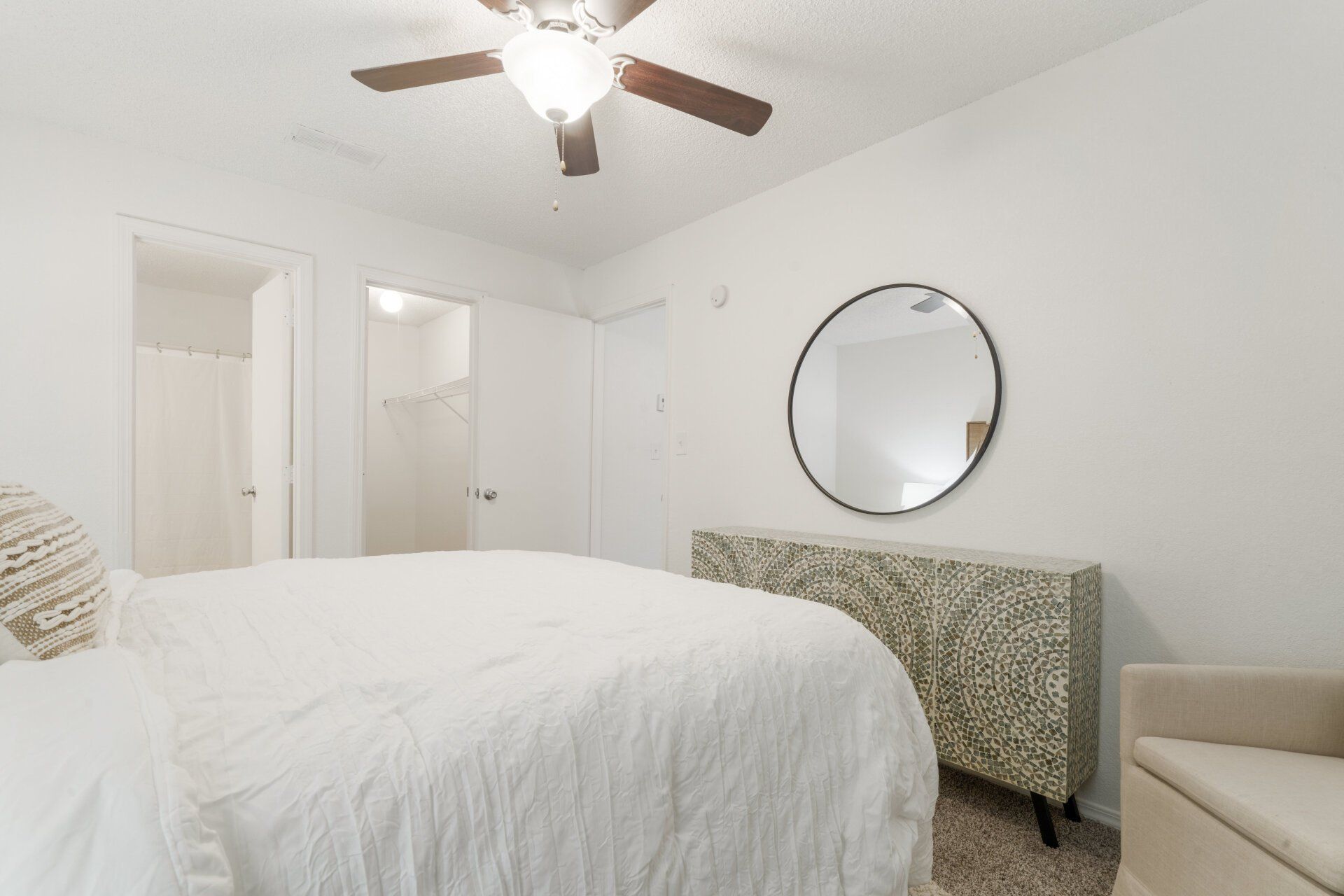 A bedroom with a bed , dresser , mirror and ceiling fan.