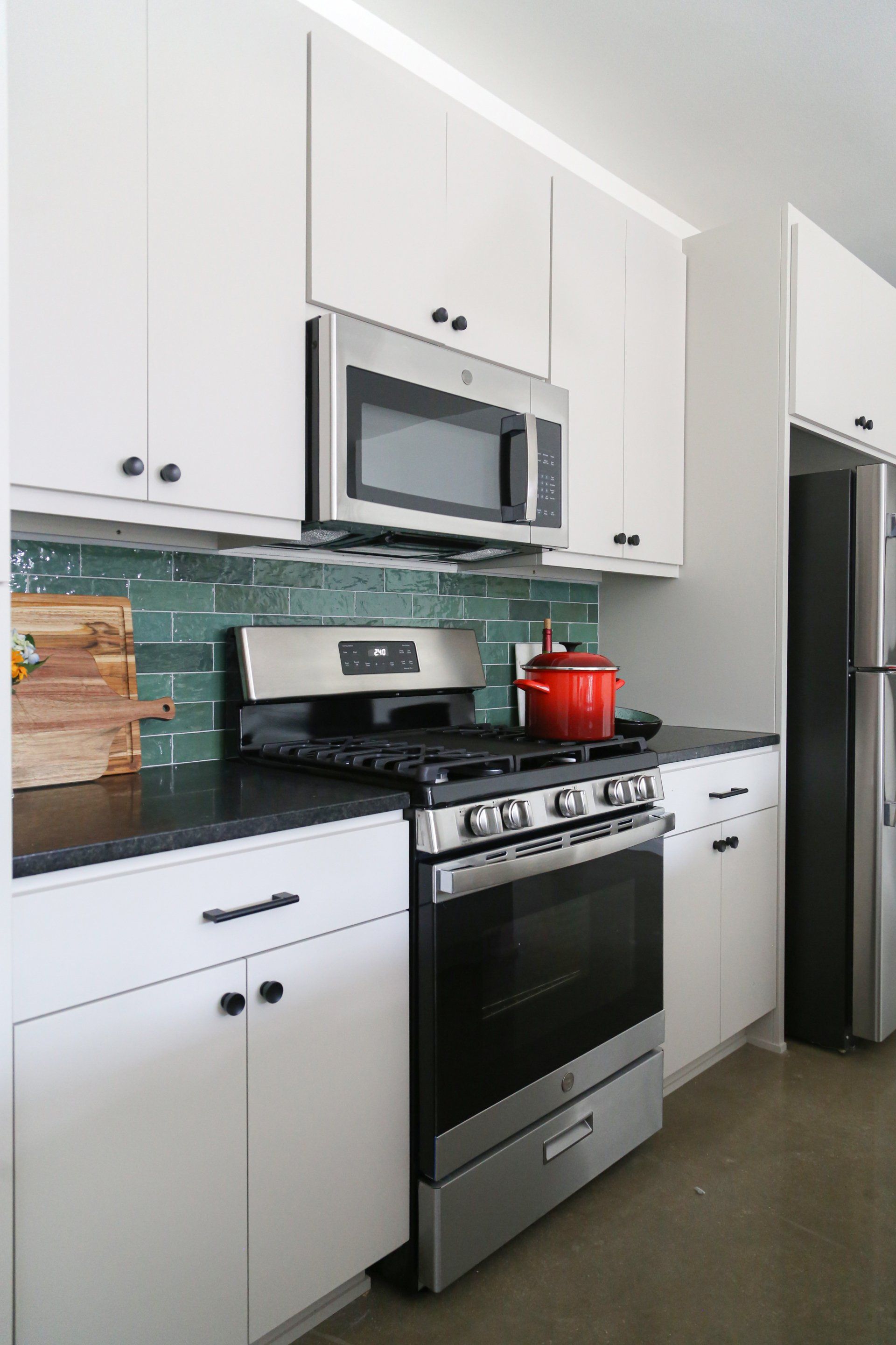 A kitchen with a stove , microwave , refrigerator and white cabinets.