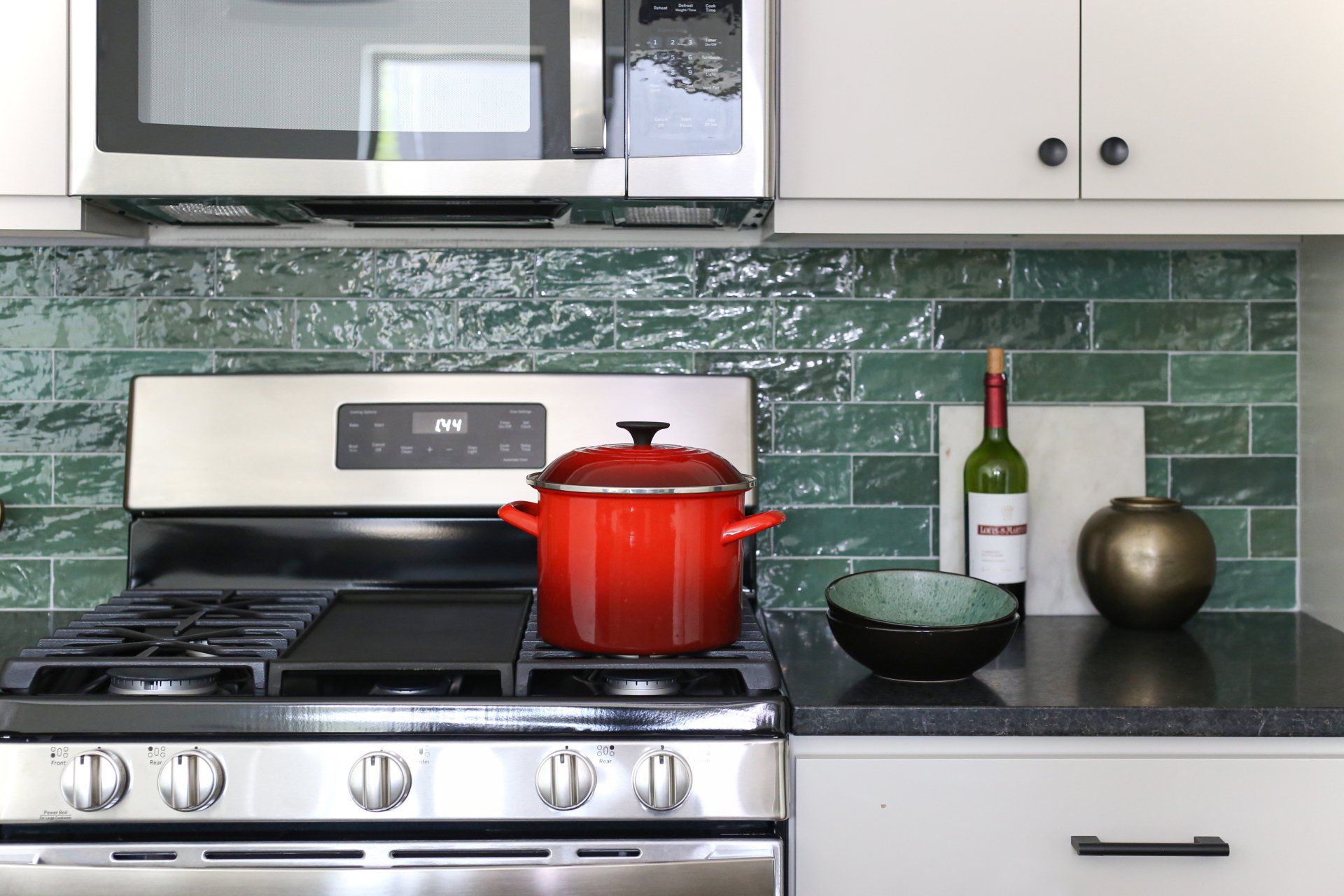 A kitchen with a pot on the stove and a bottle of wine on the counter.