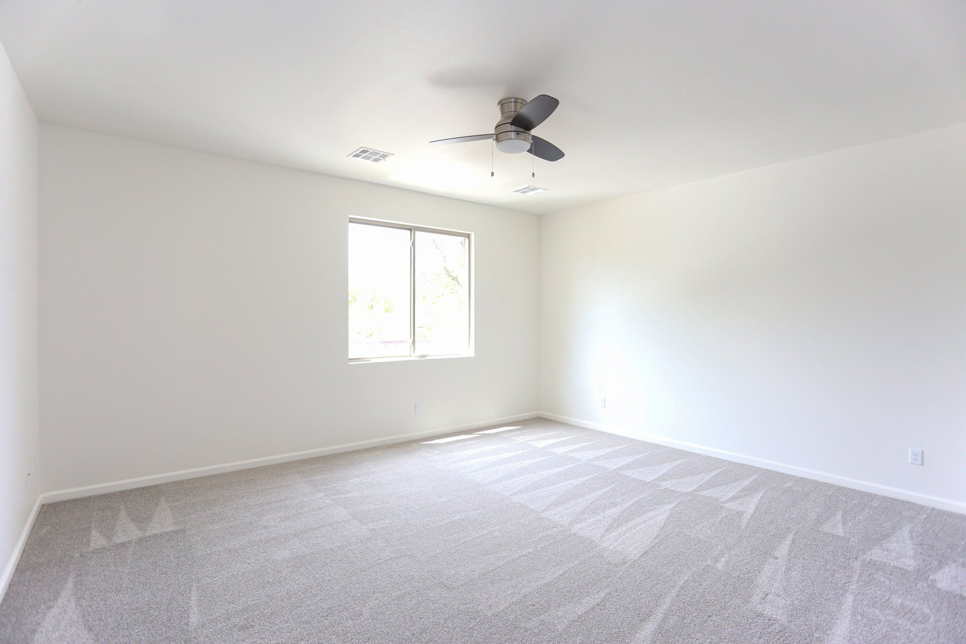 An empty bedroom with a ceiling fan and a window.