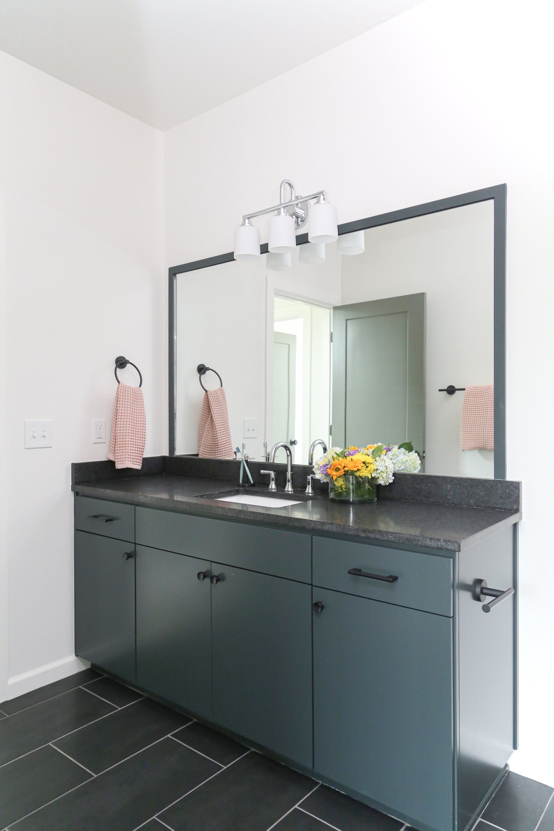 A bathroom with two sinks , two mirrors , and a black tile floor.