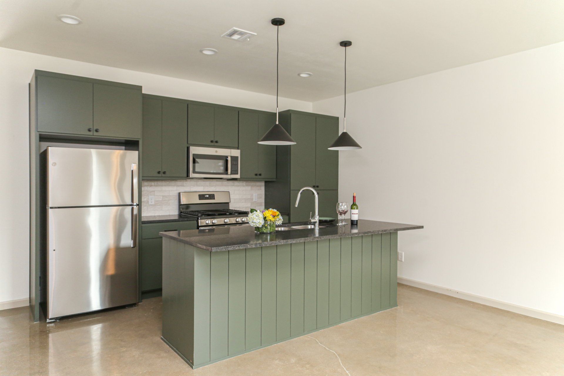A kitchen with green cabinets , stainless steel appliances and a large island.