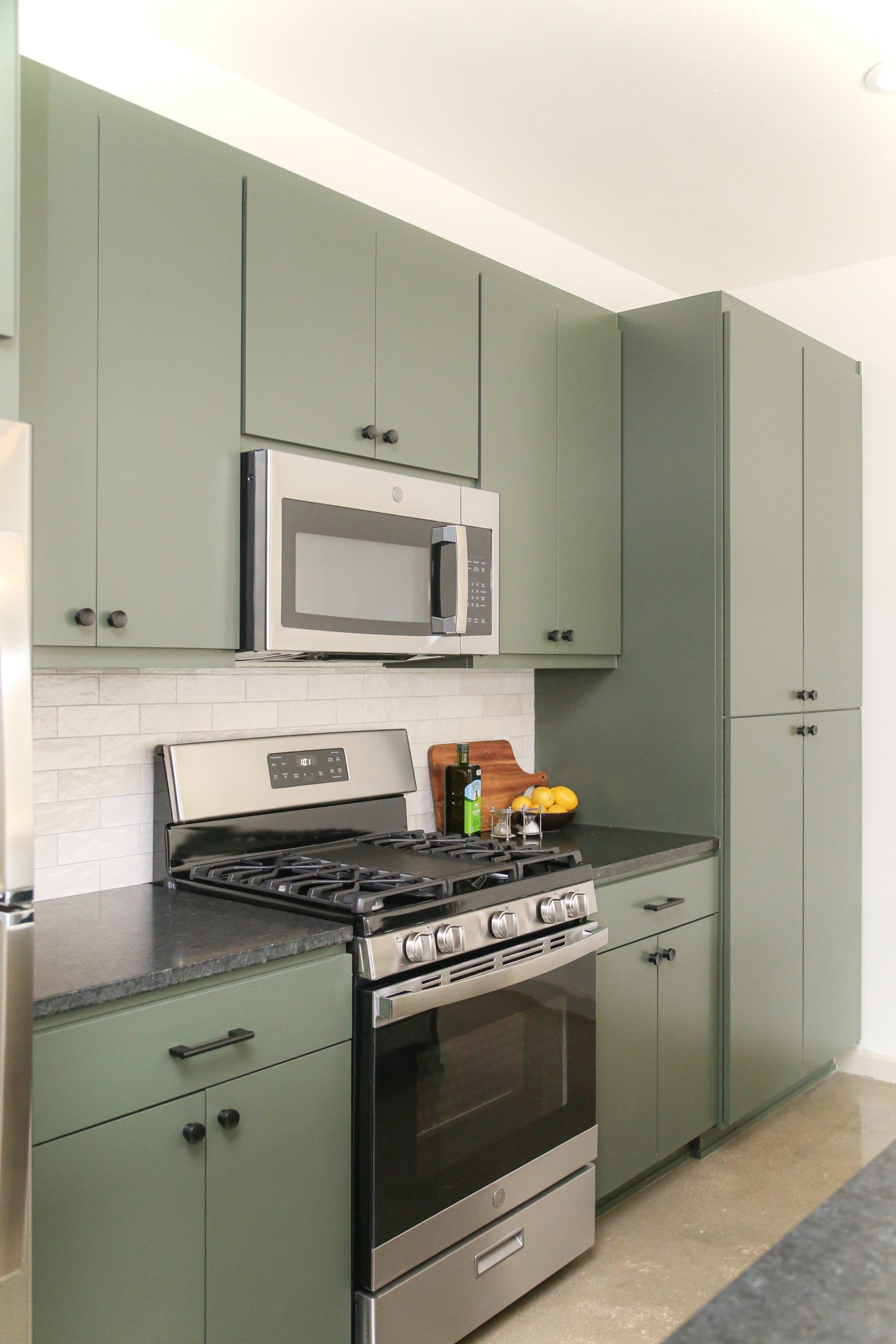 A kitchen with green cabinets , a stove , a microwave , and a refrigerator.