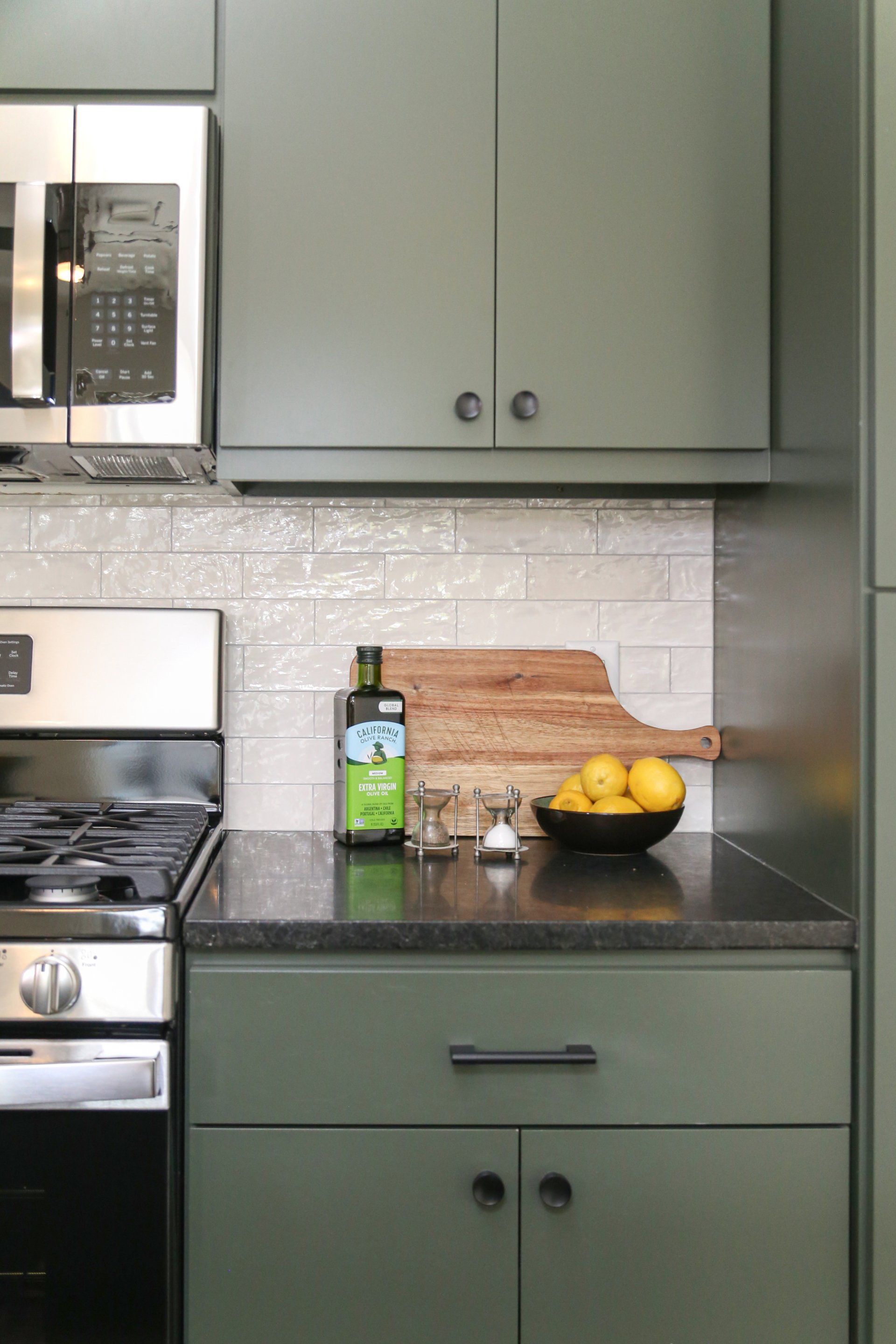 A kitchen with green cabinets and a bottle of olive oil on the counter